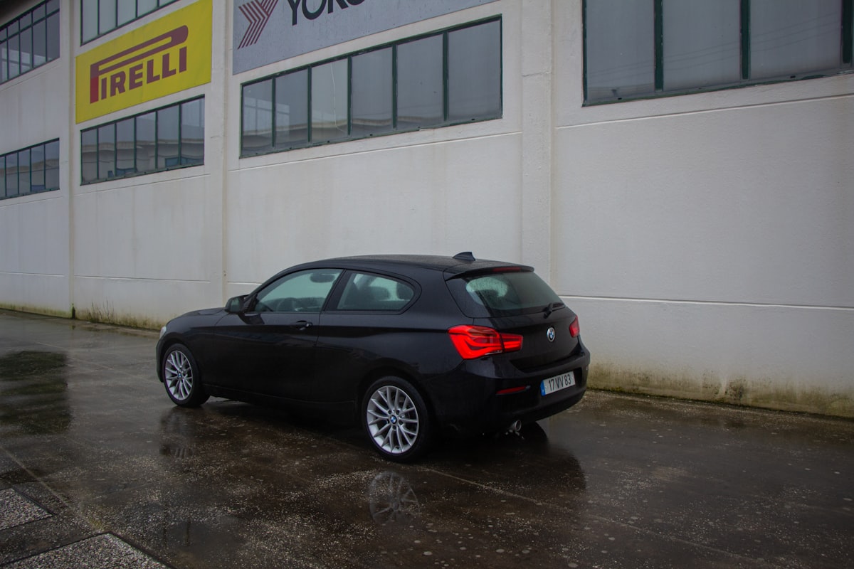 Um BMW preto estacionado em uma rua molhada.